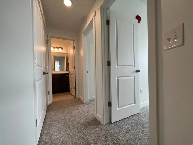 Hallway with light colored carpet and baseboards