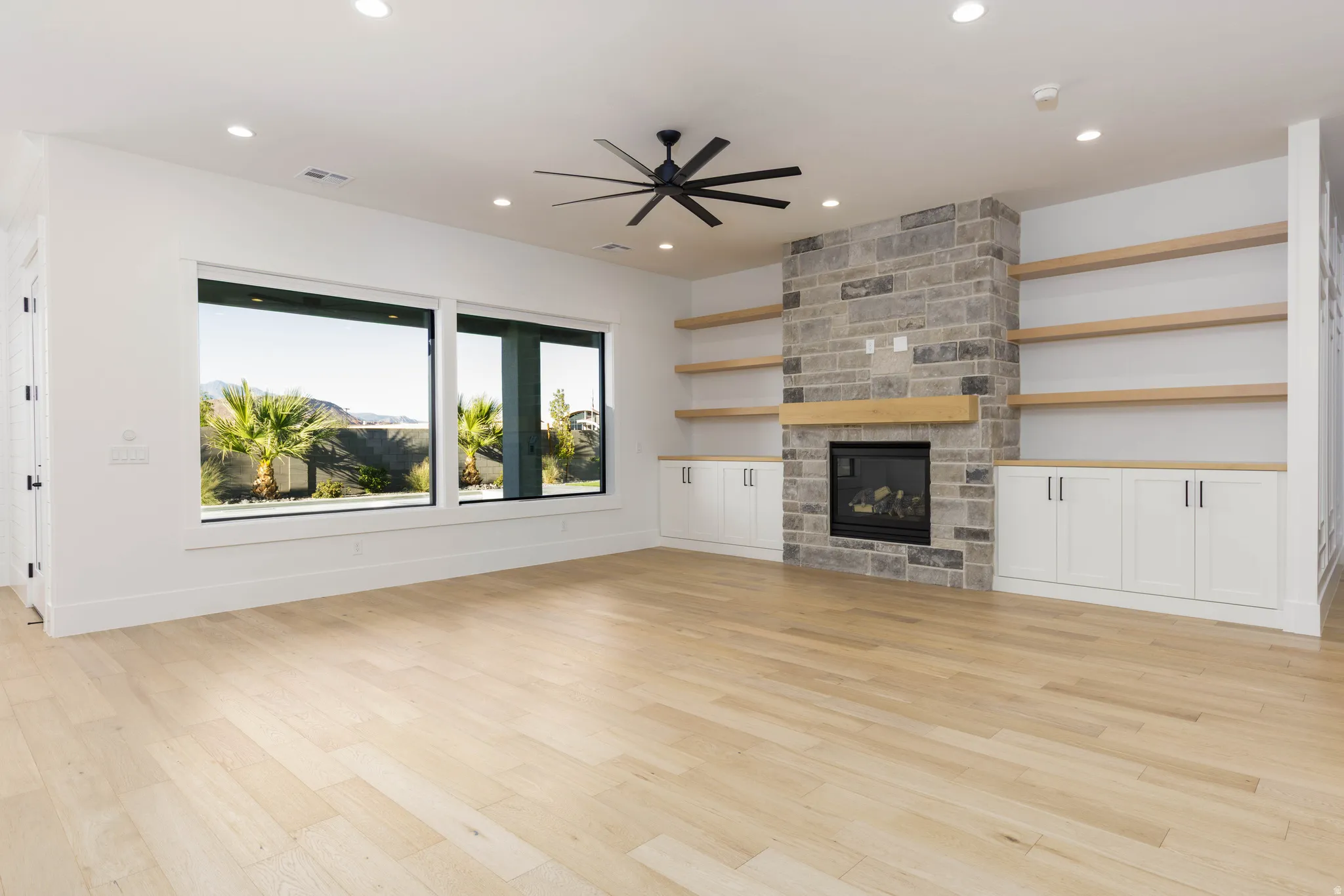 Unfurnished living room featuring a ceiling fan, a stone fireplace, light wood finished floors, and recessed lighting