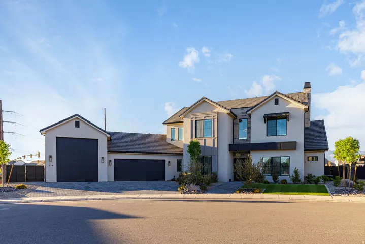 View of front of home with stucco siding, a garage, driveway, and a chimney