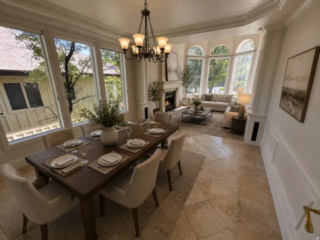 Open-concept dining and living area featuring large bay windows, a built-in fireplace with a stone surround, and elegant crown molding AI-staged or enhanced