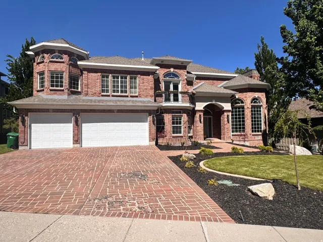 Brick exterior featuring a multi-car garage with white doors, an arched entry, and a large brick paver driveway