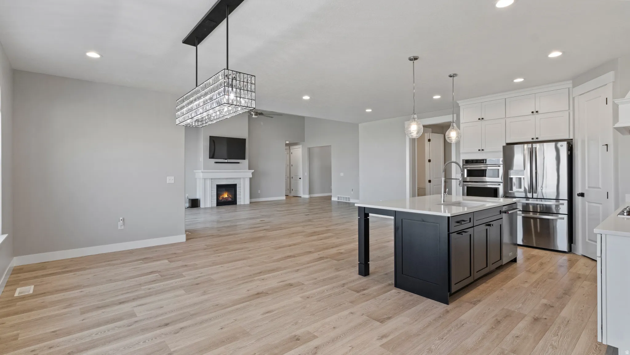 Kitchen with two tone cabinets, open floor plan, stainless steel appliances, a warm lit fireplace, and a center island with sink