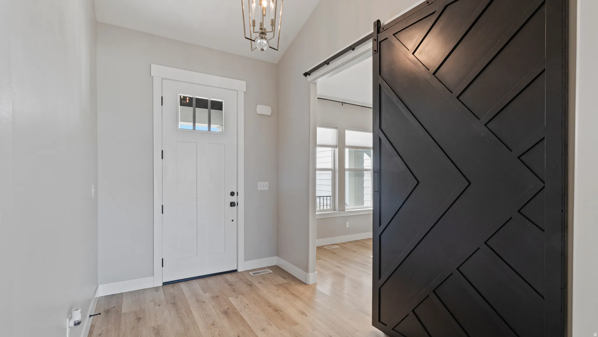 Foyer entrance featuring lofted ceiling, a barn door, light wood-type flooring, and suspended lighting