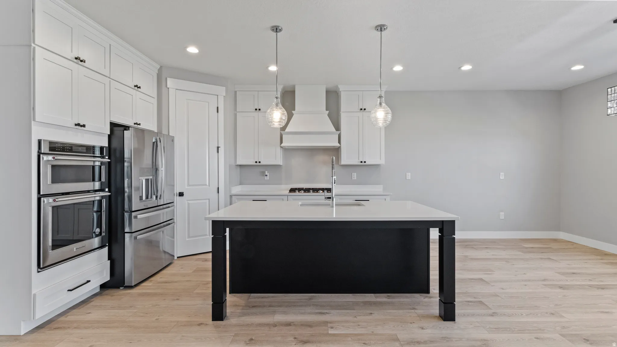 Two tone kitchen with stainless steel appliances, light wood-type flooring, an island with sink, pendant lighting, and two tone cabinets