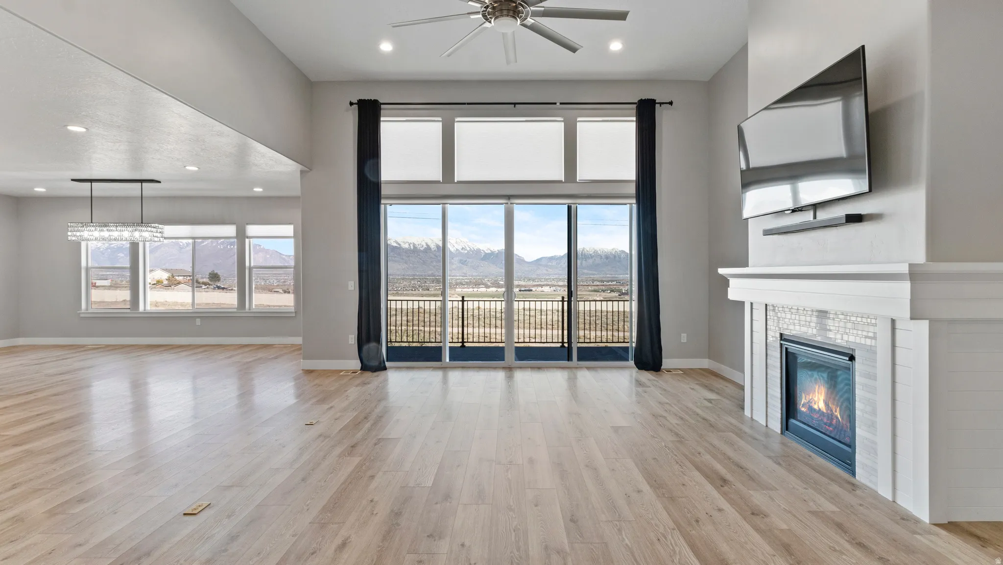 Unfurnished living room featuring a fireplace, light wood-style flooring, a ceiling fan, recessed lighting, and a high ceiling