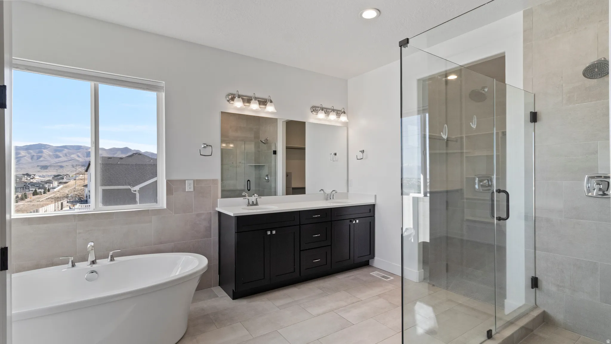Full bath featuring a shower stall, double vanity, a freestanding bath, light tile patterned floors, and tile walls