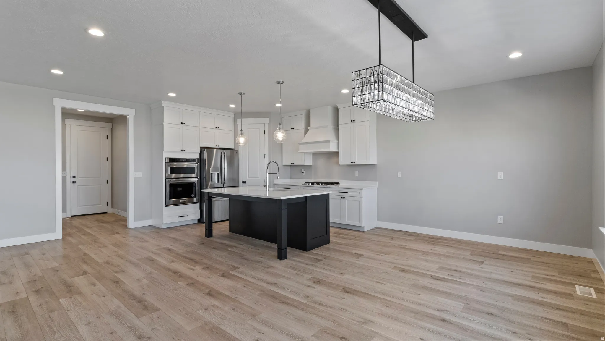 Two tone kitchen with a breakfast bar area, stainless steel appliances, a kitchen island with sink, two tone color scheme, and light wood finished floors