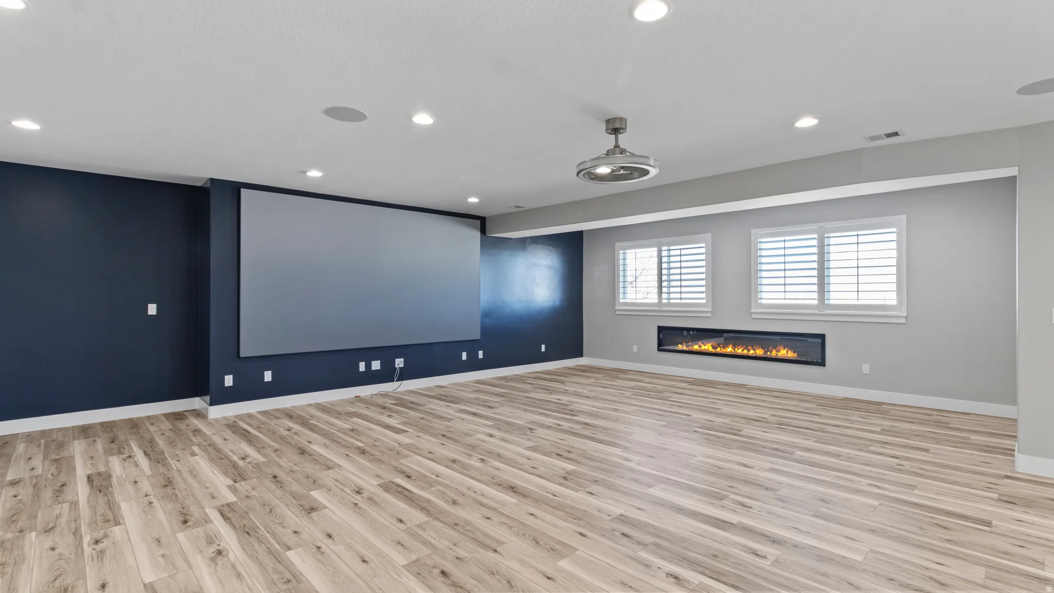 Home theater room featuring light wood finished floors, a glass covered fireplace, and recessed lighting
