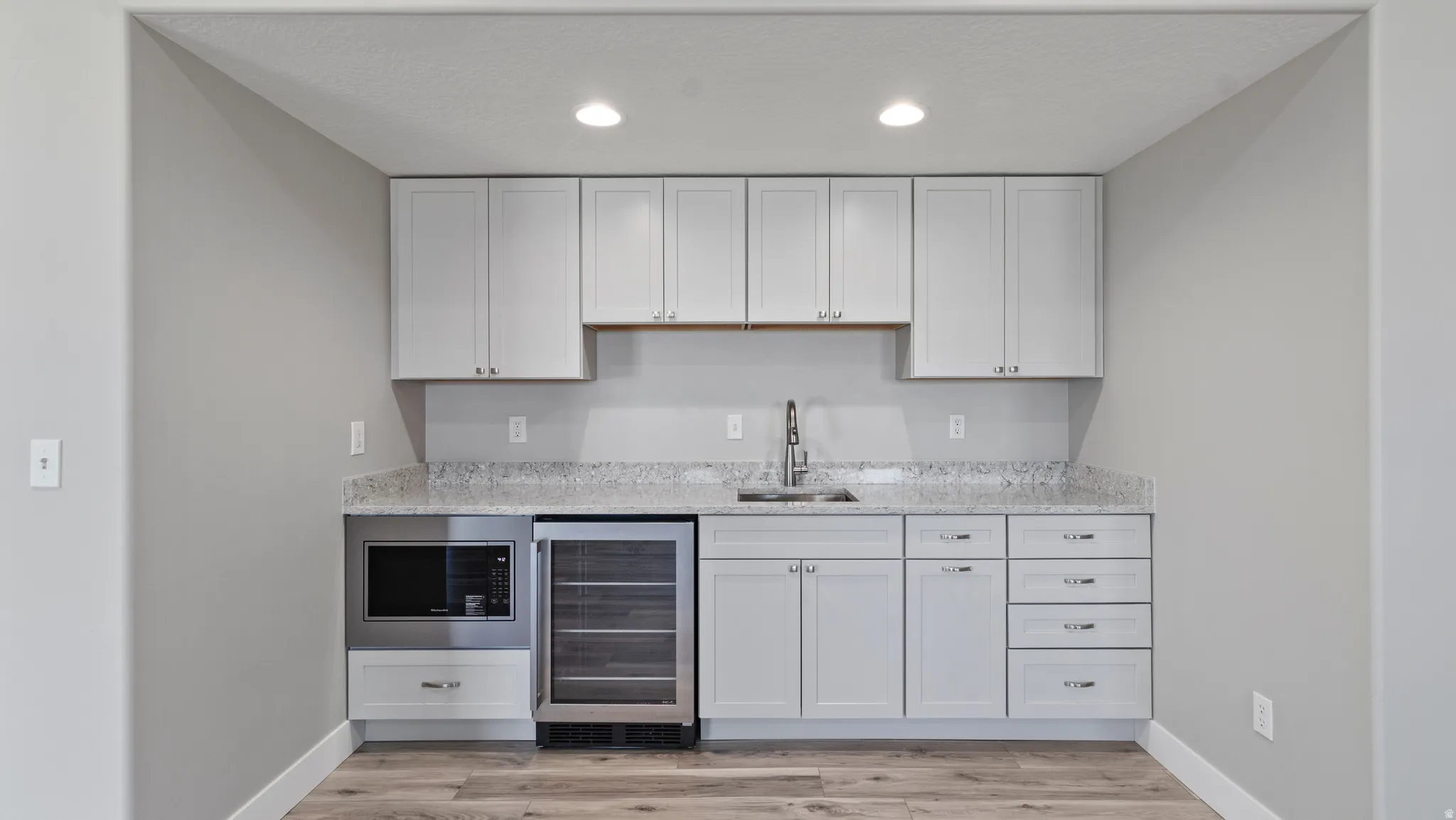 Indoor wet bar featuring light stone counters, beverage cooler, light wood-type flooring, white cabinetry, and recessed lighting