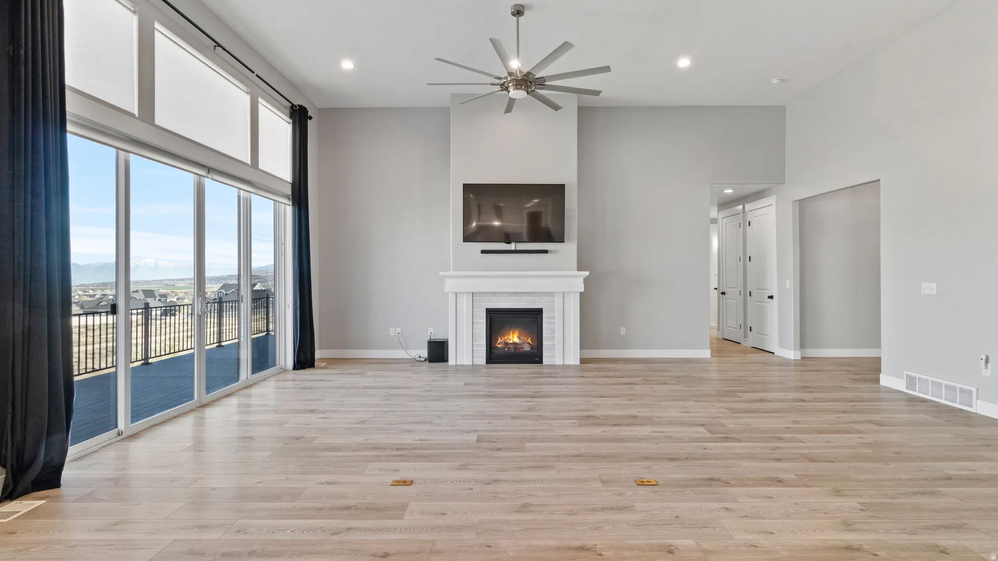 Unfurnished living room with a high ceiling, a ceiling fan, a lit fireplace, light wood-type flooring, and recessed lighting