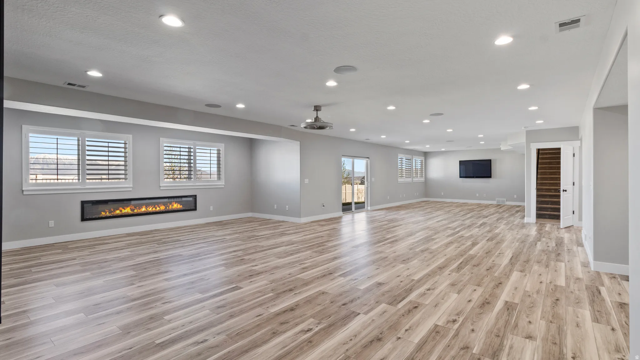 Unfurnished living room with a glass covered fireplace, ceiling fan, light wood-style flooring, and recessed lighting