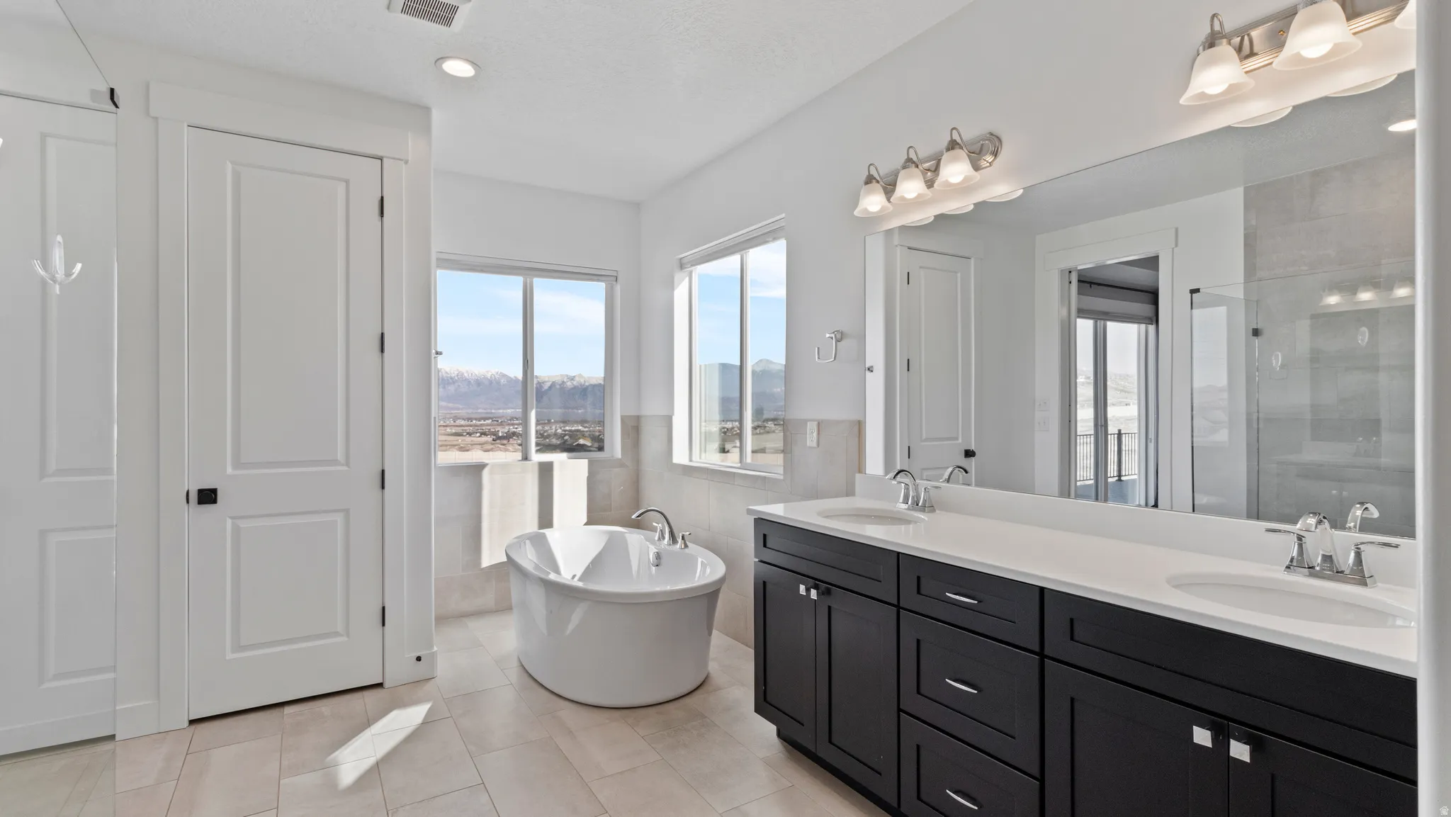 Bathroom featuring double vanity, tile walls, a soaking tub, a wainscoted wall, and tiled shower
