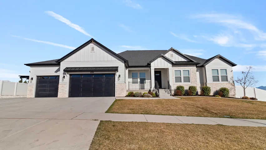 Modern farmhouse style home with stone siding, a standing seam roof, a garage, driveway, and board and batten siding