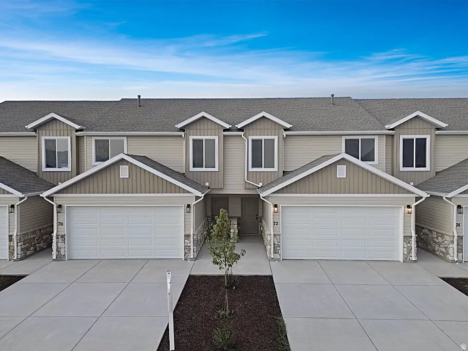 Townhome exterior featuring light-colored siding, a dark shingle roof, and stone facade accents