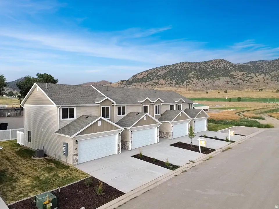 Modern townhome-style residences featuring light-toned siding, attached garages, and a mountainous backdrop