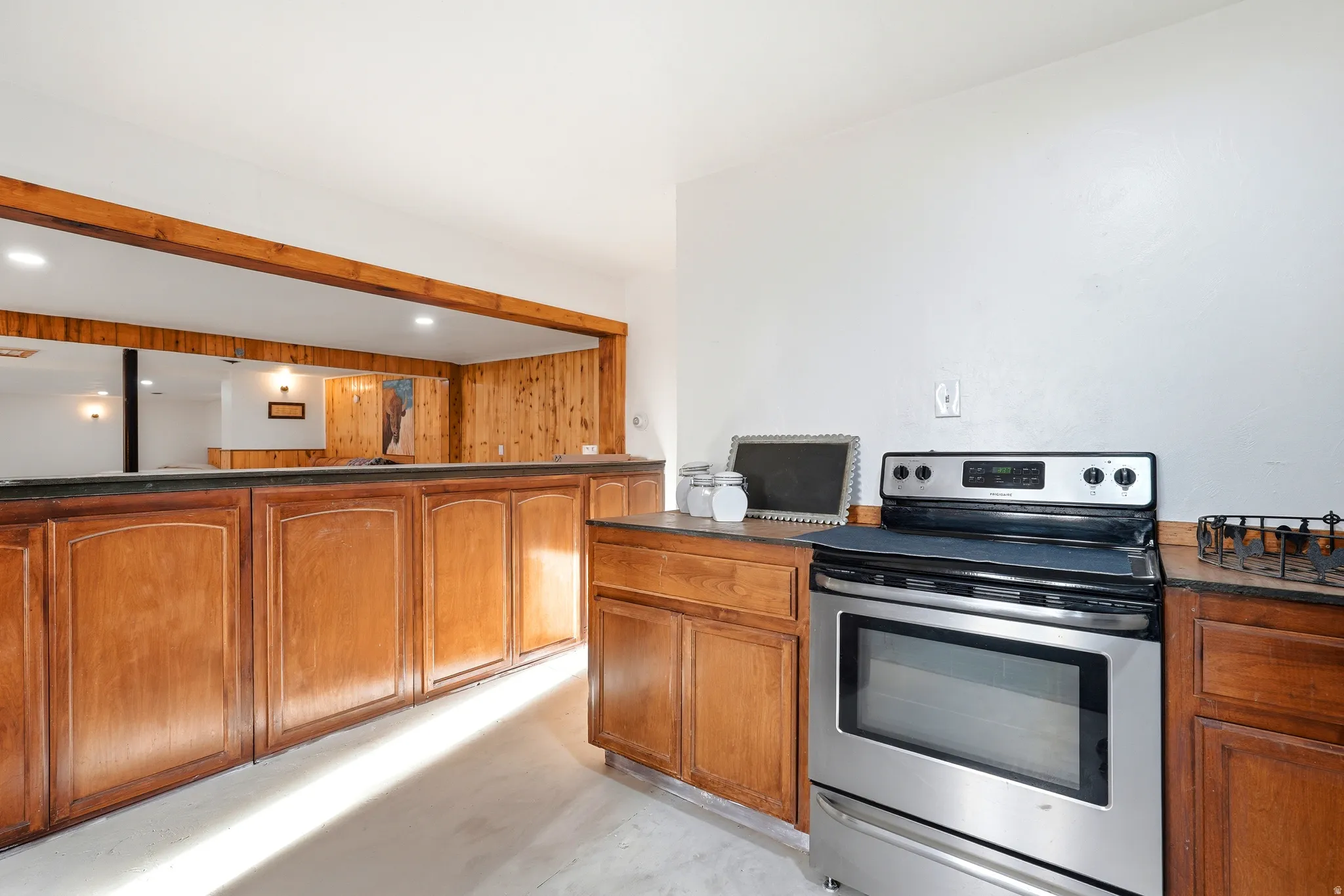 Kitchen featuring stainless steel electric range oven, wood finish cabinetry, dark countertops, finished concrete floors, and recessed lighting