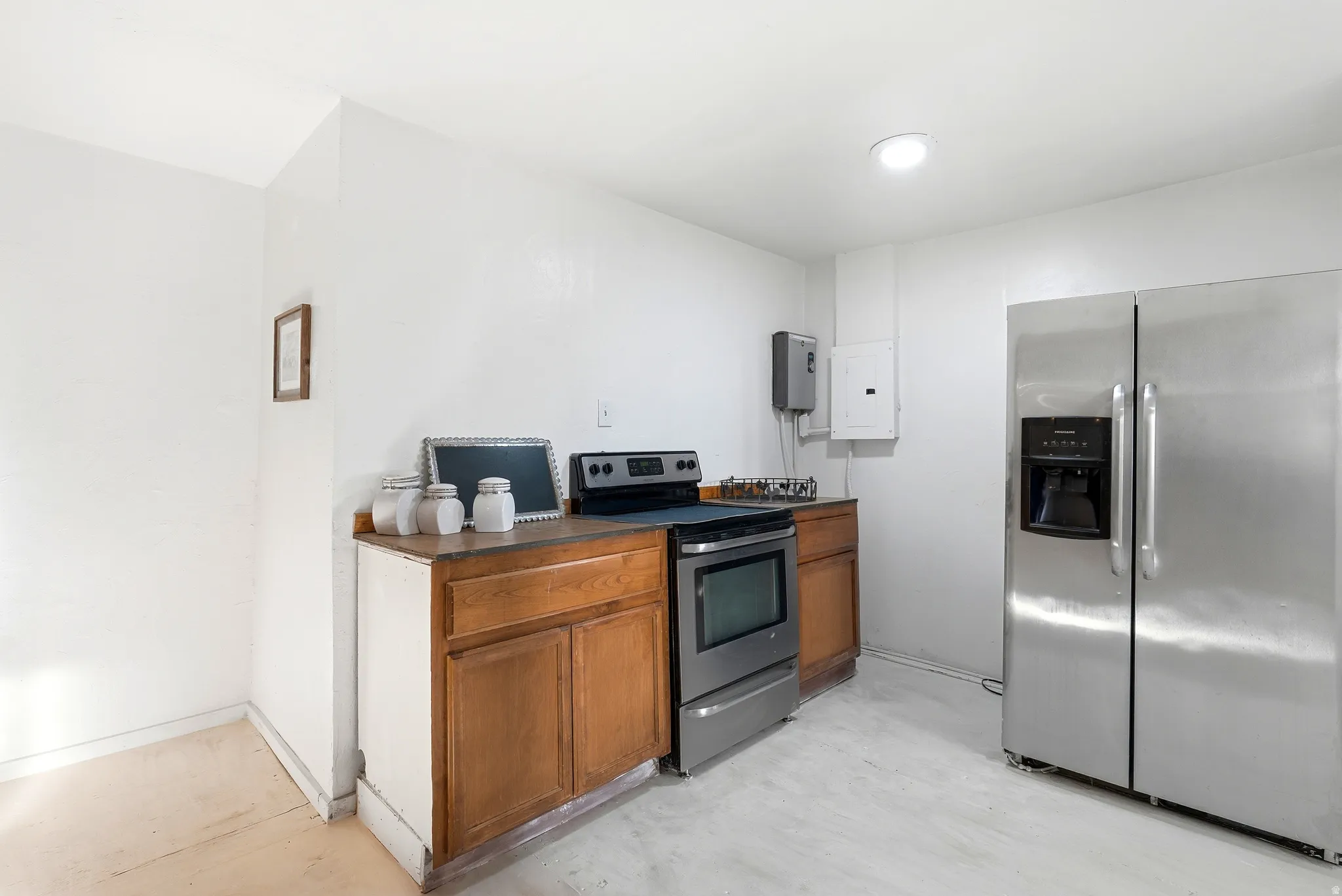 Kitchen with stainless steel appliances, wood finish cabinetry, dark countertops, electric panel, and concrete flooring