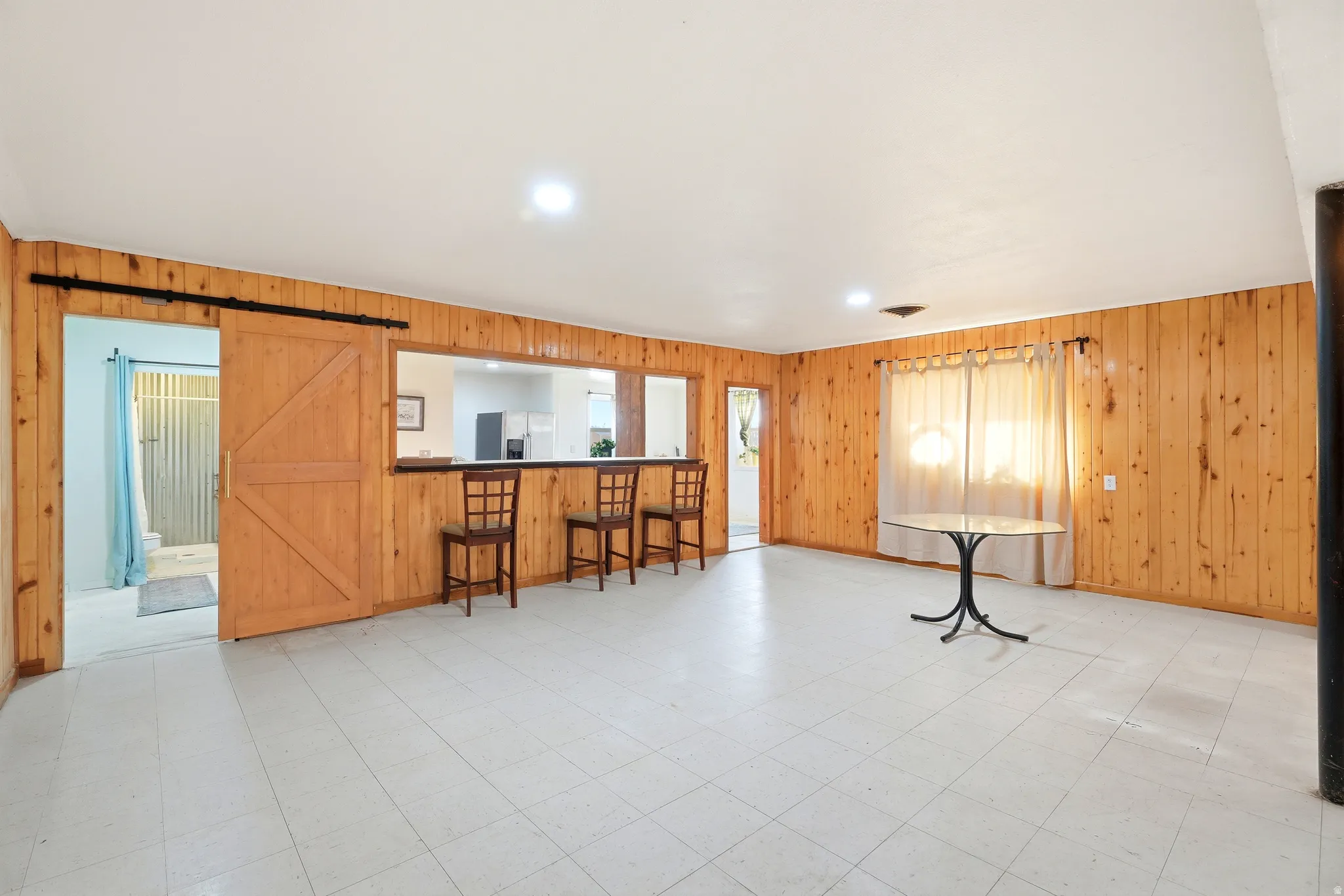Living room with a barn door, light floors, recessed lighting, and wood walls