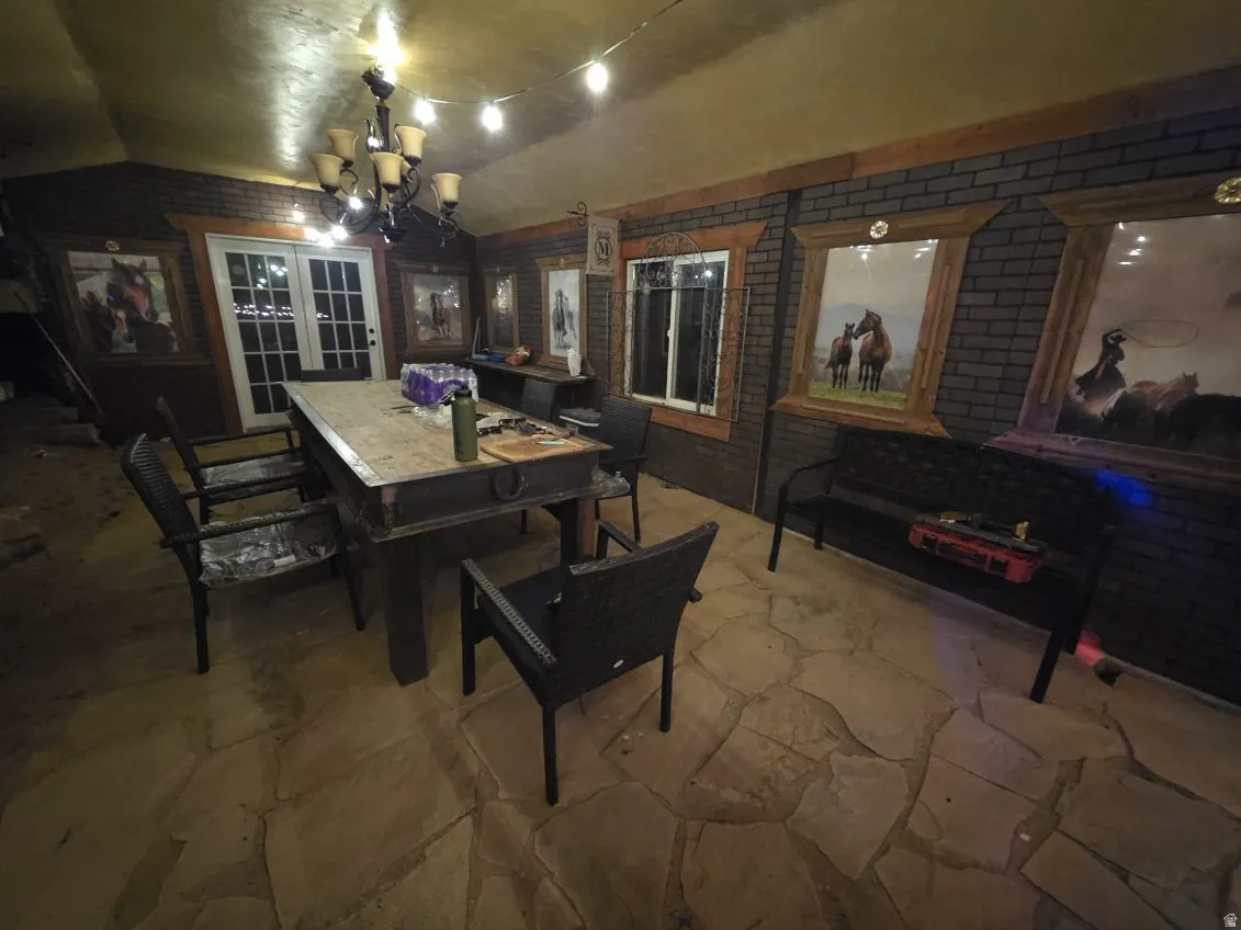 Dining area with brick wall, a chandelier, stone floors, and vaulted ceiling