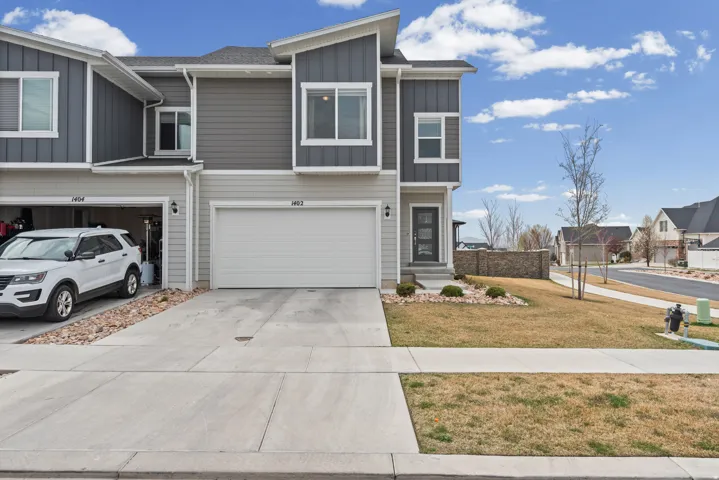 View of front of property with board and batten siding, driveway, a garage, a front lawn, and a residential view