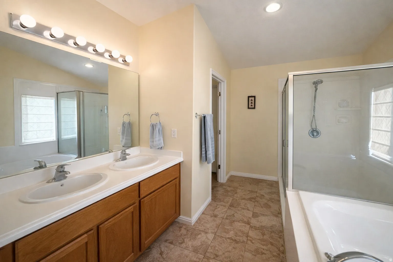 Full bathroom with a bath, double vanity, a stall shower, recessed lighting, and vaulted ceiling