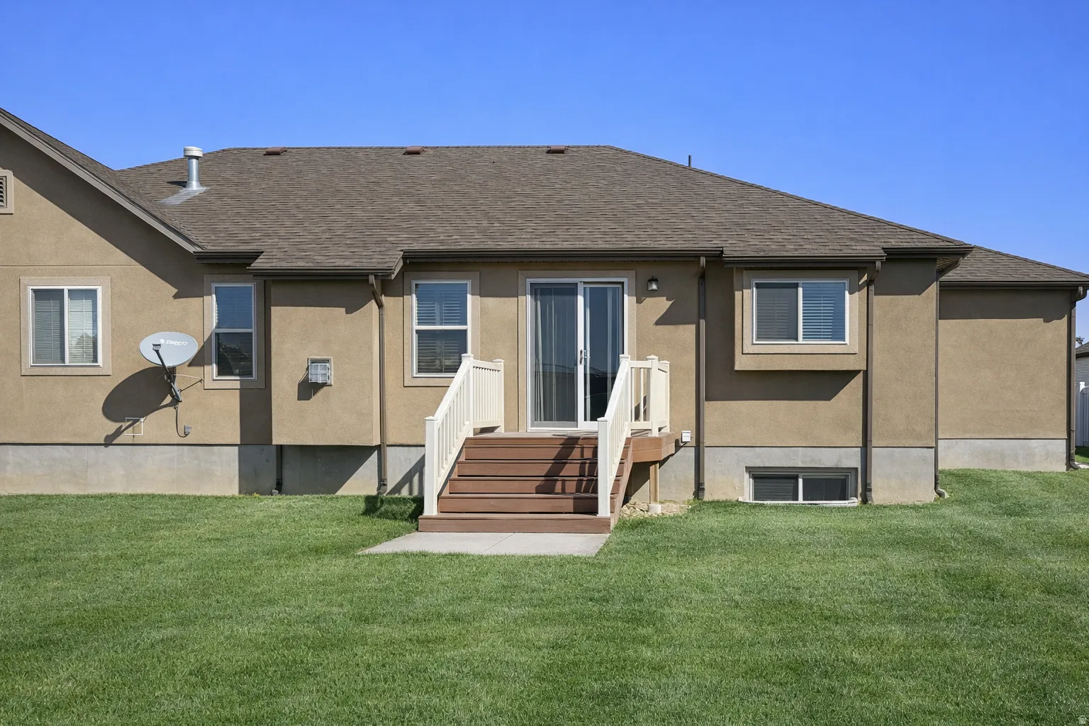Rear view of property with a yard, stucco siding, and a shingled roof