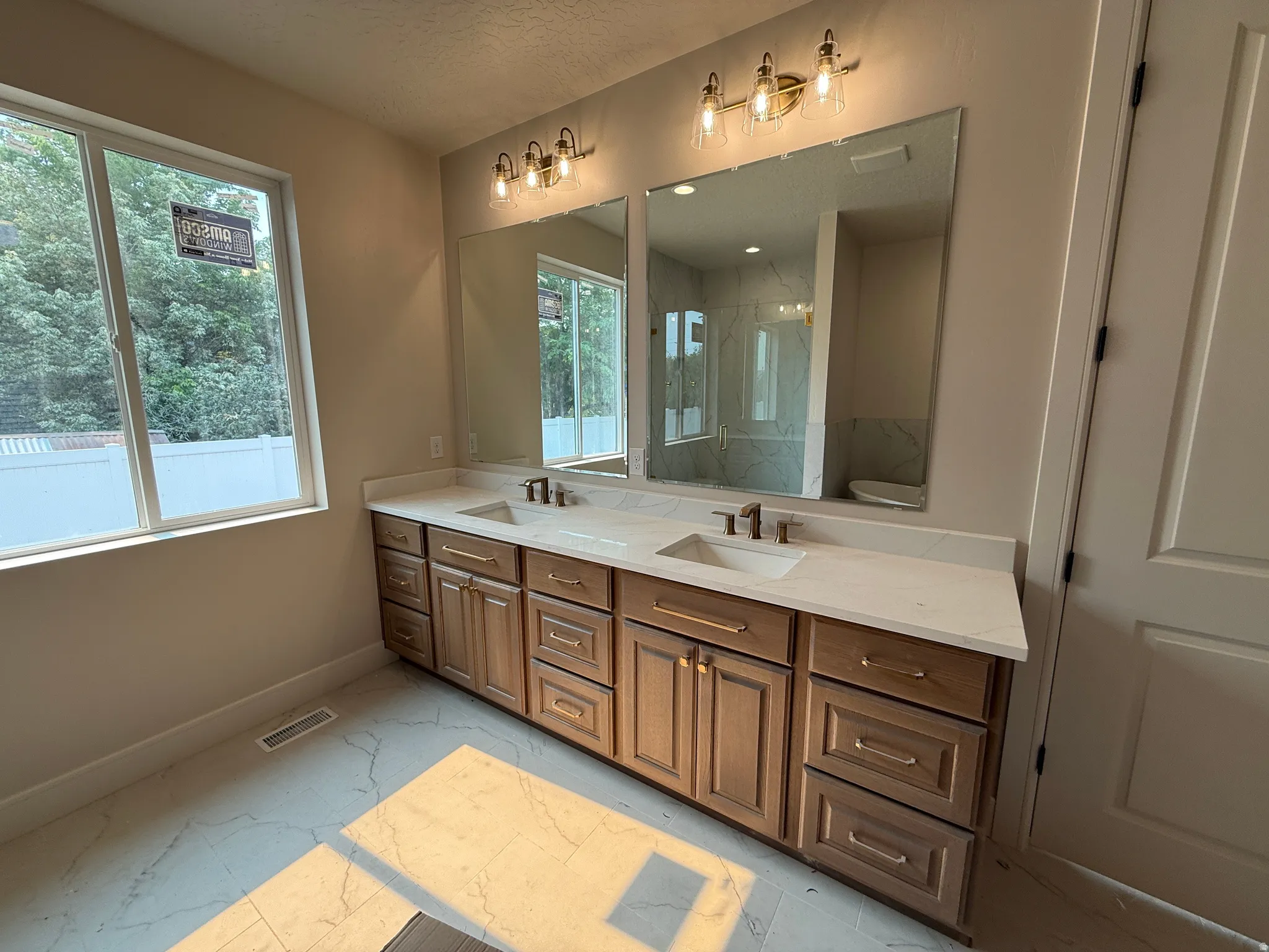 Double vanity with light wood-finish cabinetry, gold hardware, and white countertops