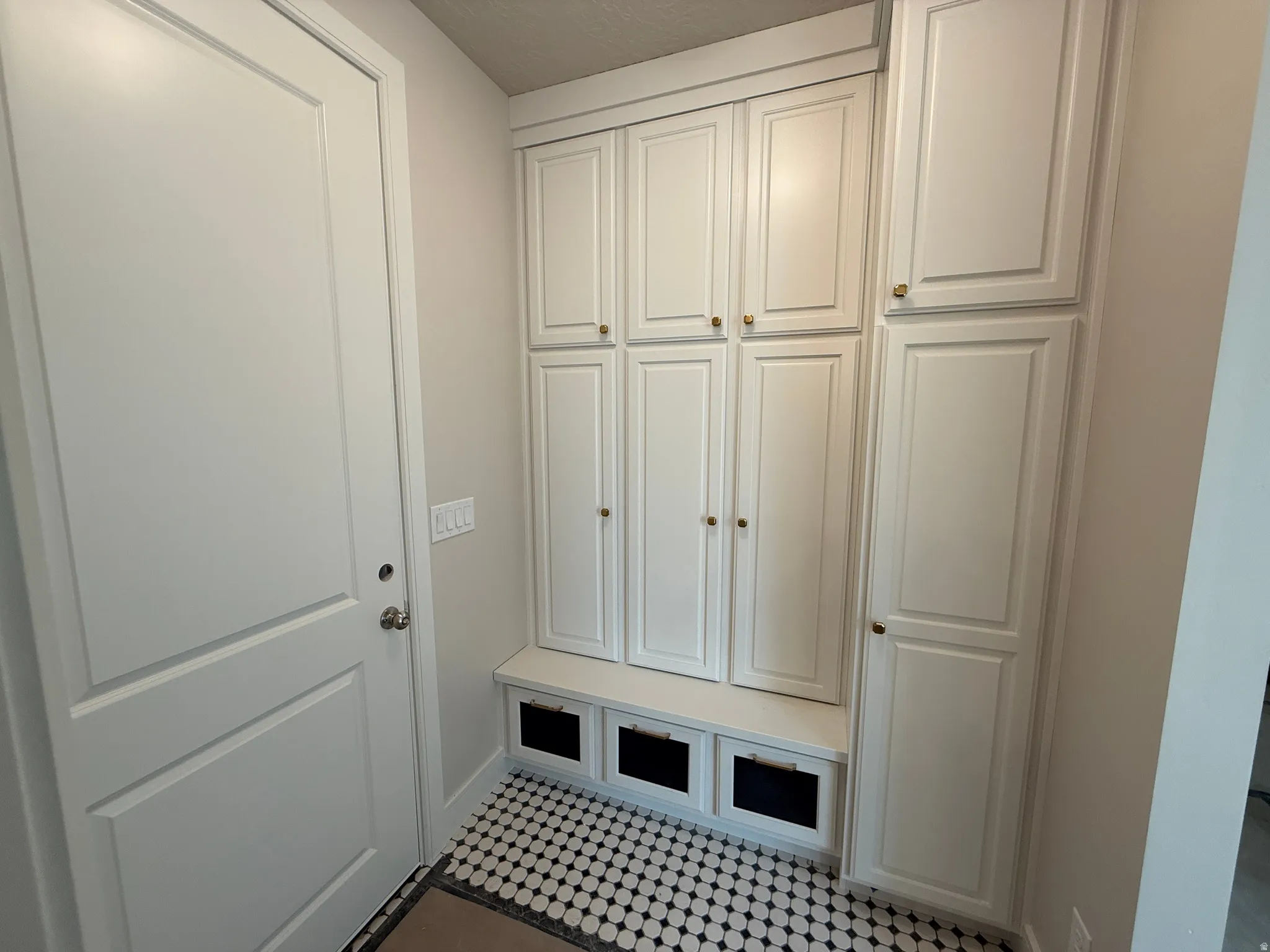 Built-in mudroom cabinetry with a bench and three cubbies, complemented by black and white hexagonal tile flooring