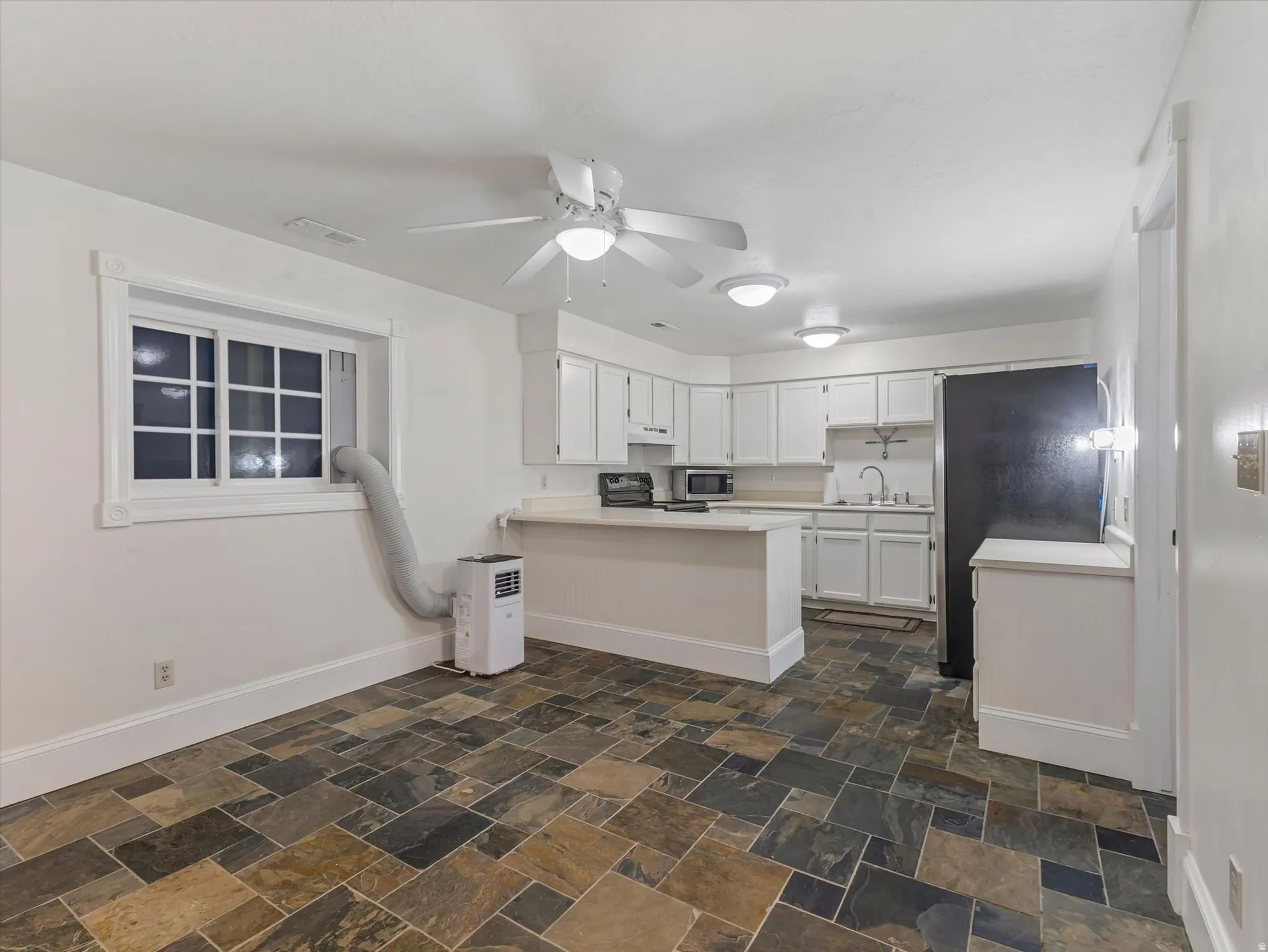 Apartment kitchen with light countertops, stainless steel appliances, white cabinets, a ceiling fan, and a peninsula