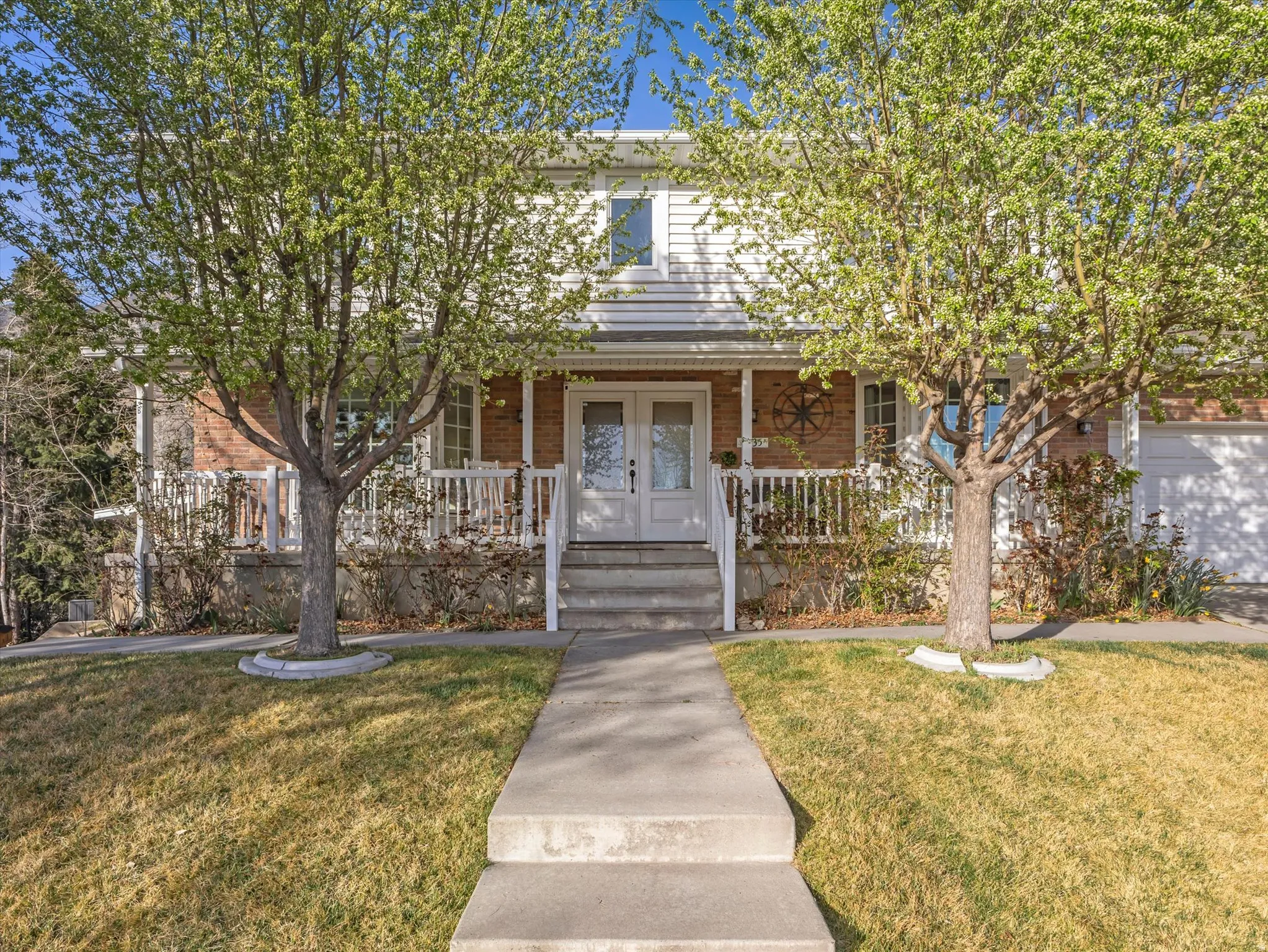 View of property hidden behind natural elements with french doors, a front yard, a porch, and brick siding