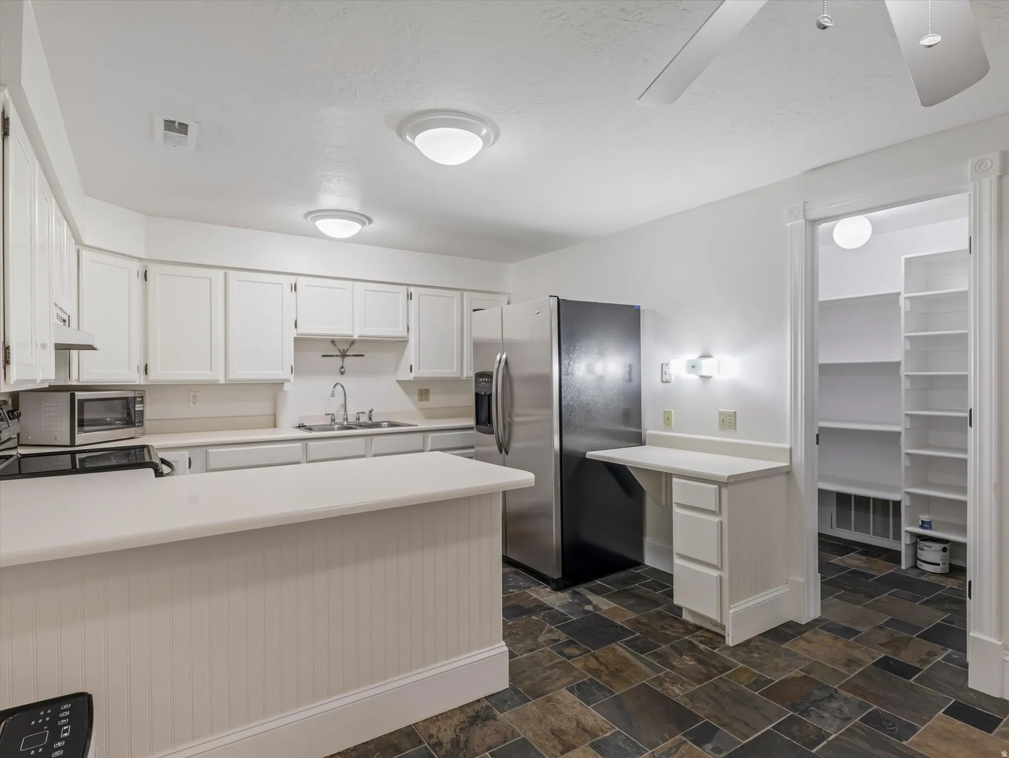 Apartment kitchen featuring white cabinets, light countertops, stainless steel appliances, a peninsula, and dark stone finish flooring