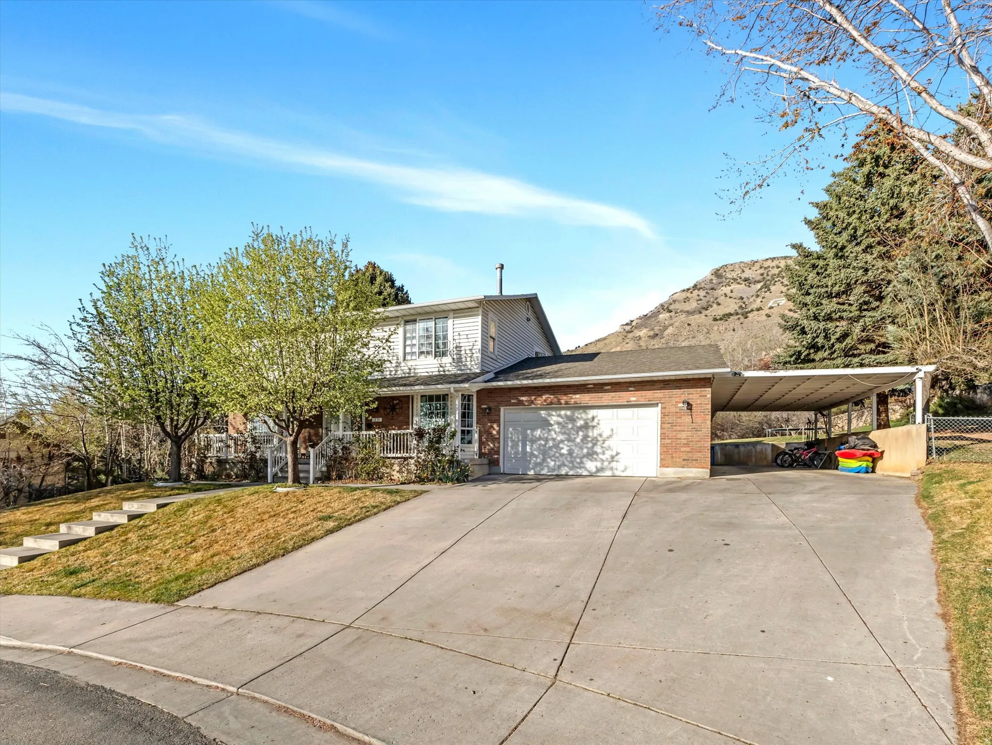 View of front of property with an attached carport, brick siding, an attached garage, driveway, and covered porch