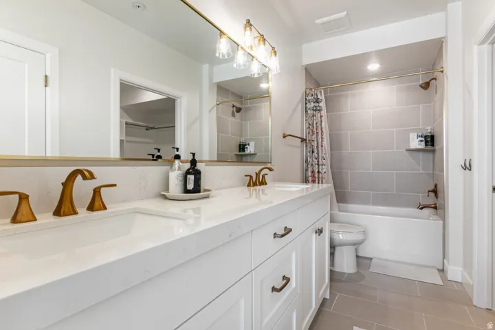 Full bathroom featuring double vanity, shower / bath combination with curtain, and light tile patterned floors
