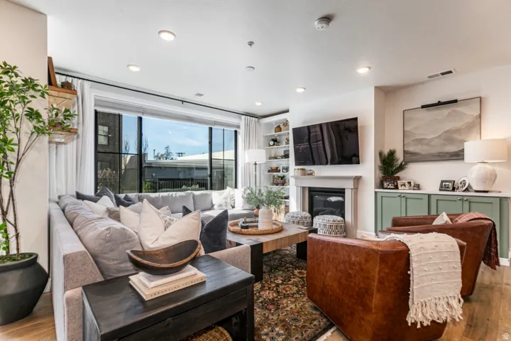 Living area with wood finished floors, a glass covered fireplace, and recessed lighting