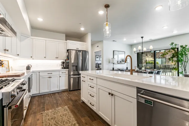 Kitchen with stainless steel appliances, white cabinetry, dark wood-type flooring, light stone countertops, and a chandelier