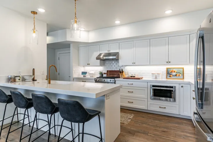Kitchen featuring a kitchen breakfast bar, dark wood-style floors, stainless steel appliances, white cabinets, and a peninsula