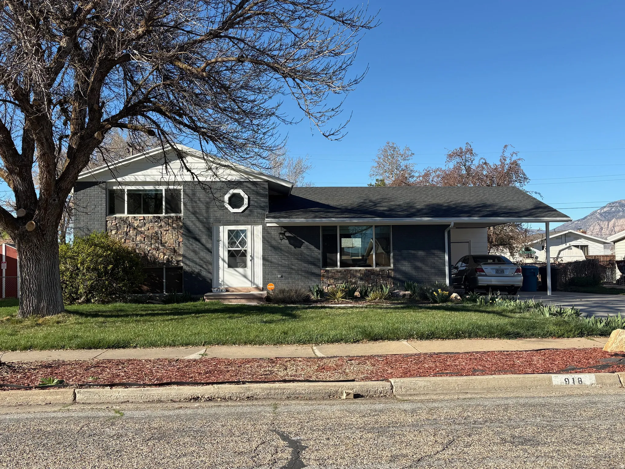 Split level home with brick siding, a carport, a front yard, a shingled roof, and driveway