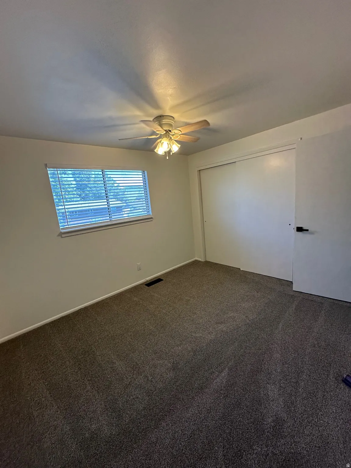 Unfurnished bedroom with dark carpet, a closet, and a ceiling fan