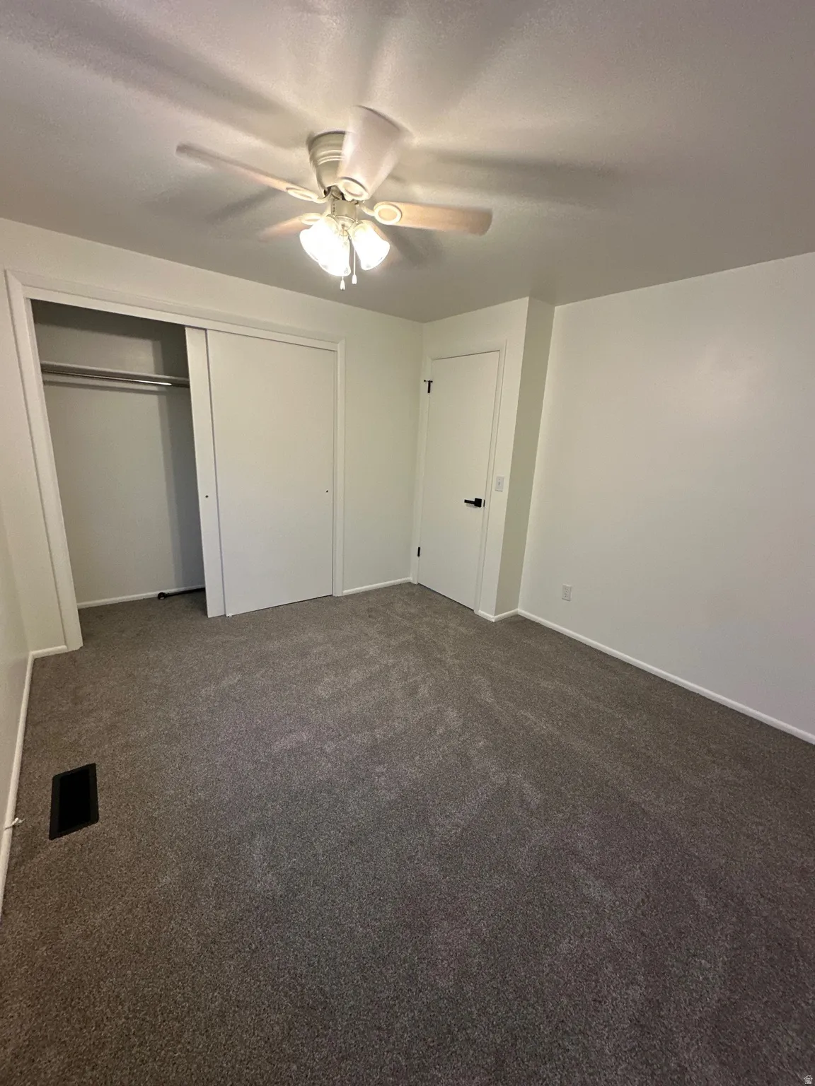 Unfurnished bedroom with dark carpet, ceiling fan, and a closet