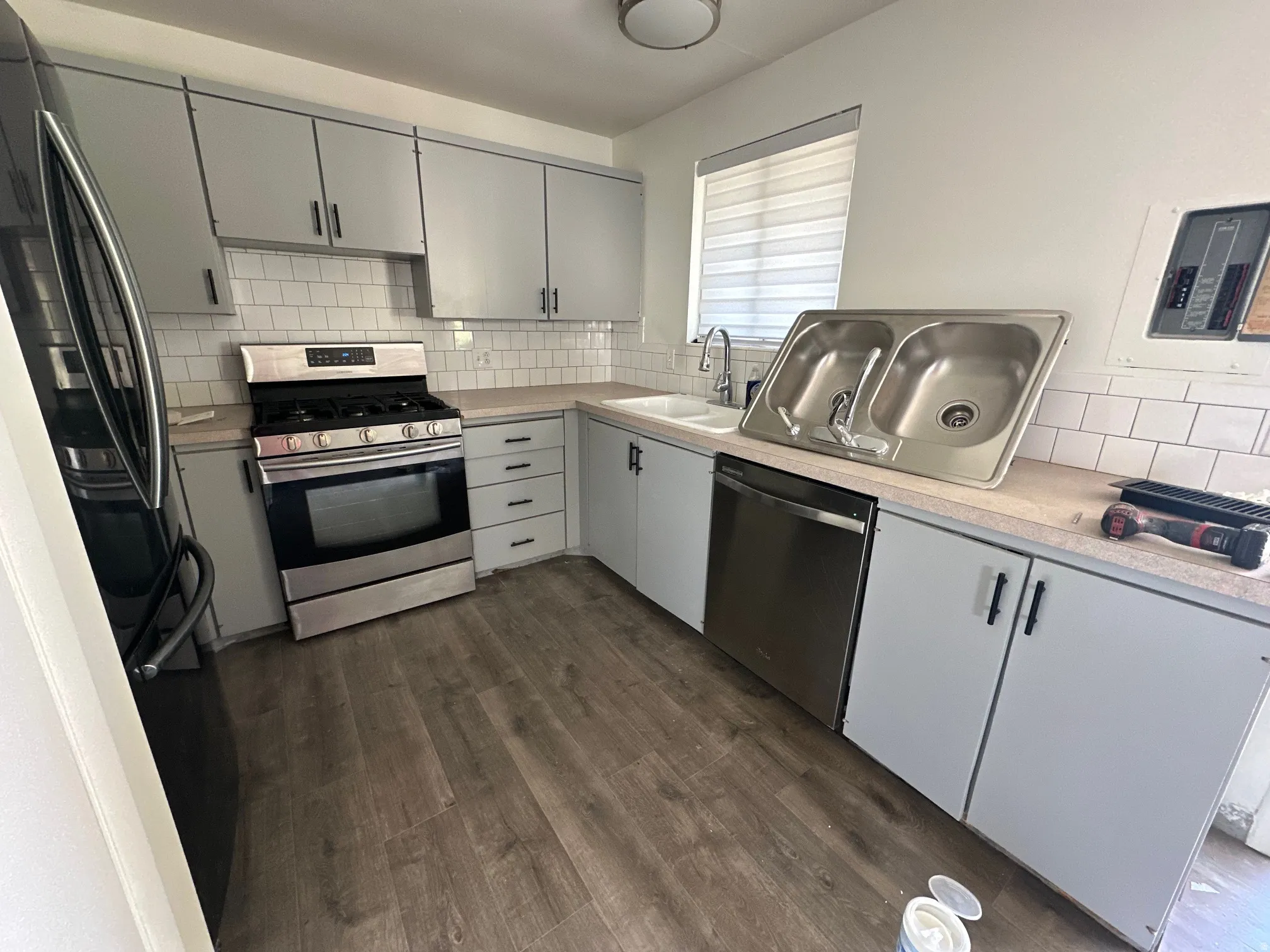 Kitchen with stainless steel appliances, gray cabinetry, light countertops, decorative backsplash, and dark wood-type flooring