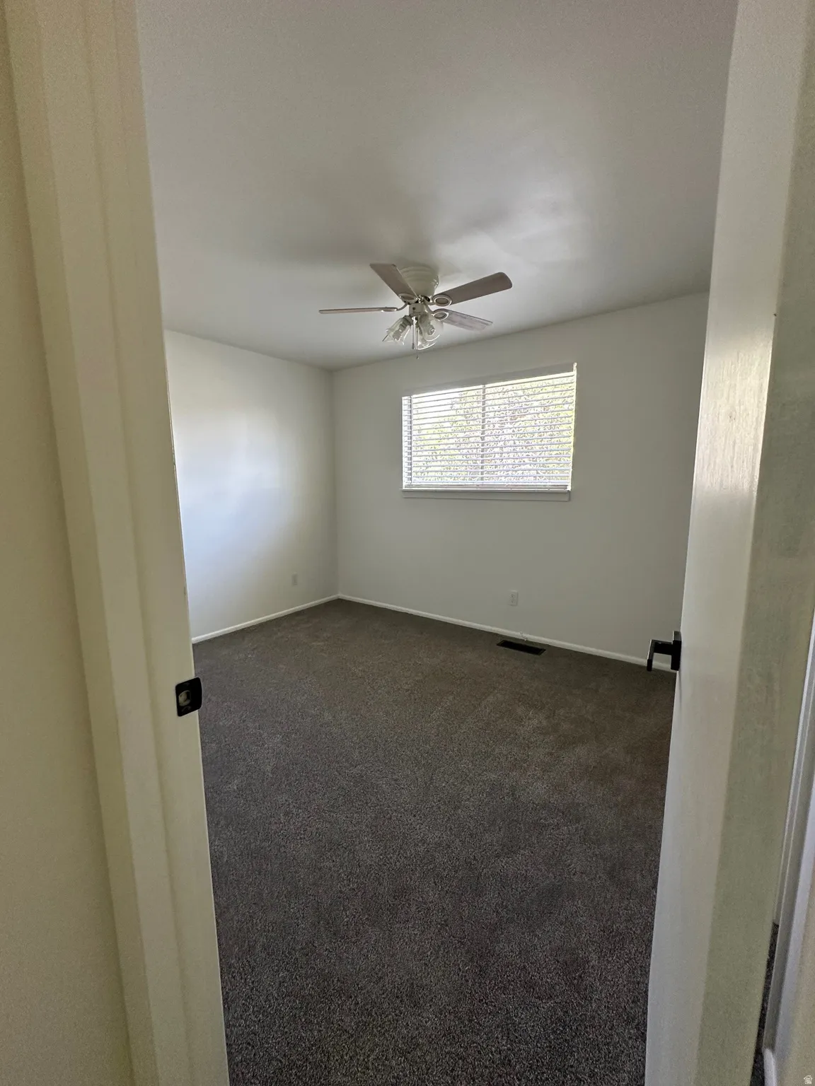 Unfurnished room featuring dark carpet and ceiling fan
