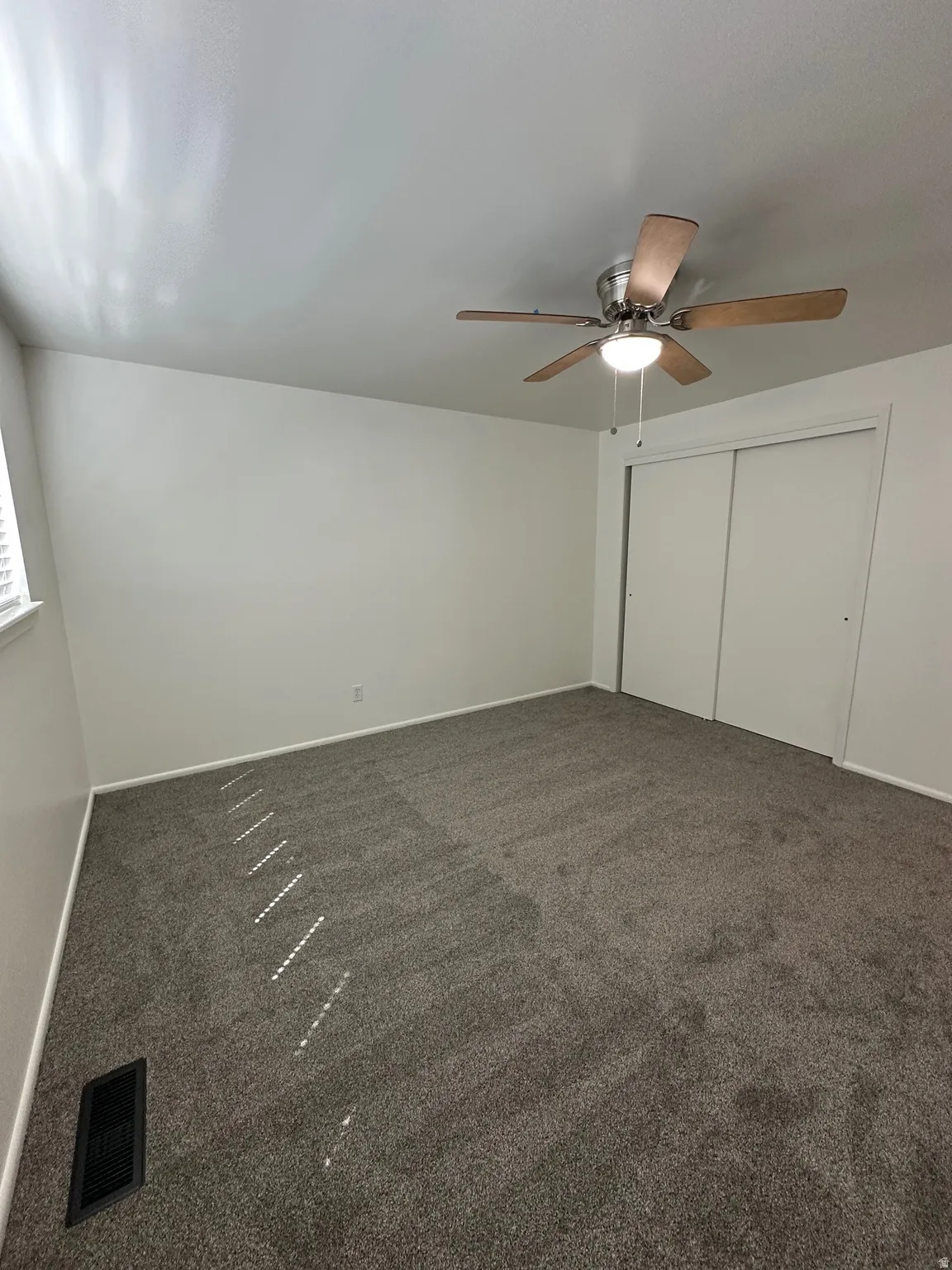 Unfurnished bedroom with a closet, dark carpet, and ceiling fan