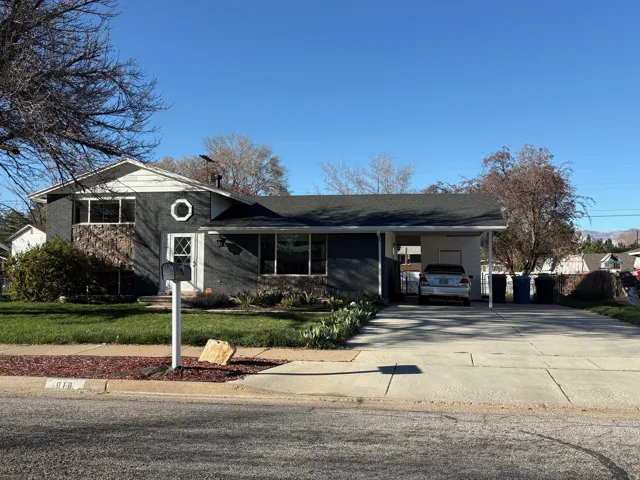 Split level home featuring an attached carport, driveway, brick siding, and a front yard