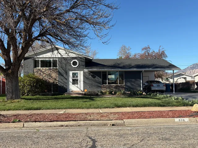 Split level home with brick siding, a carport, a front yard, a shingled roof, and driveway