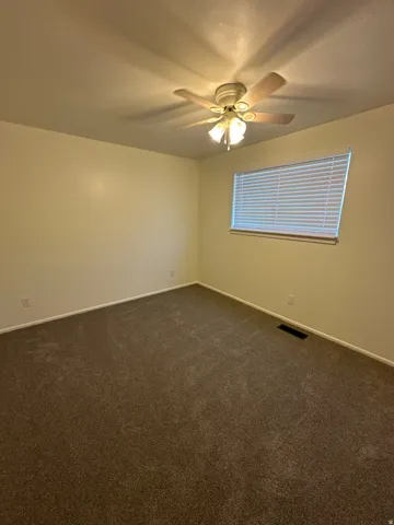 Empty room with dark colored carpet and ceiling fan