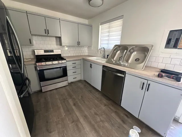 Kitchen with stainless steel appliances, gray cabinetry, light countertops, decorative backsplash, and dark wood-type flooring