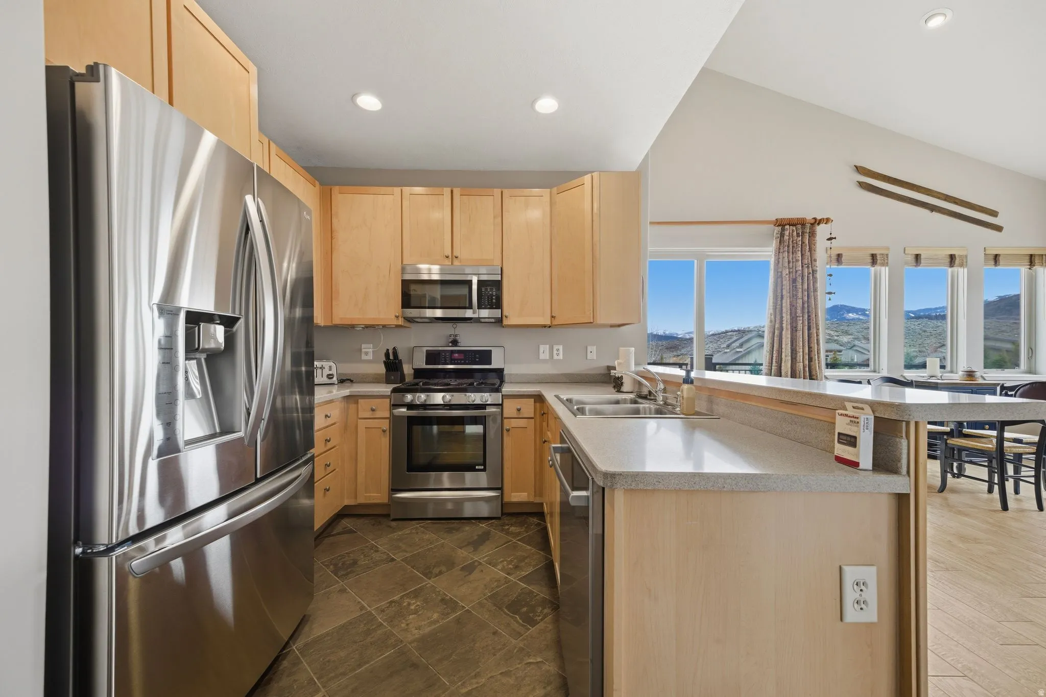 Kitchen with stainless steel appliances, a peninsula, light wood finish cabinetry, light countertops, and recessed lighting