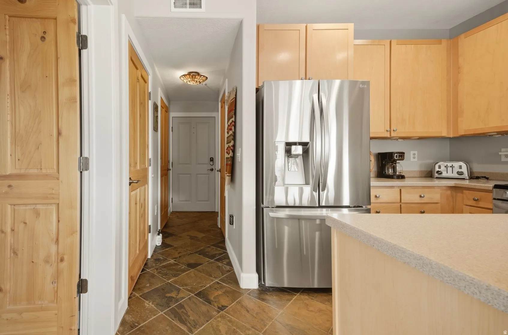 Kitchen featuring light wood finish cabinets, stainless steel fridge with ice dispenser, and dark stone finish flooring