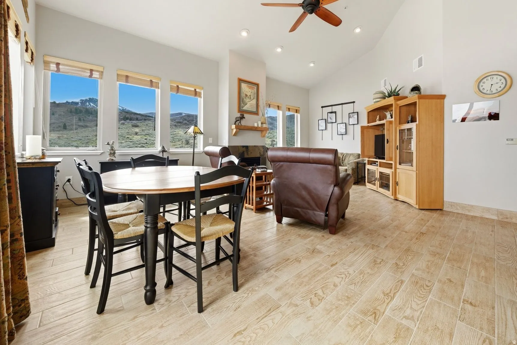 Dining area with light wood-style flooring, a ceiling fan, a fireplace, vaulted ceiling, and recessed lighting
