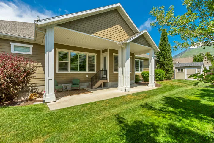 Expansive lawn with a covered patio, featuring substantial white support columns, a gray shingle roof, and a visible mountain backdrop